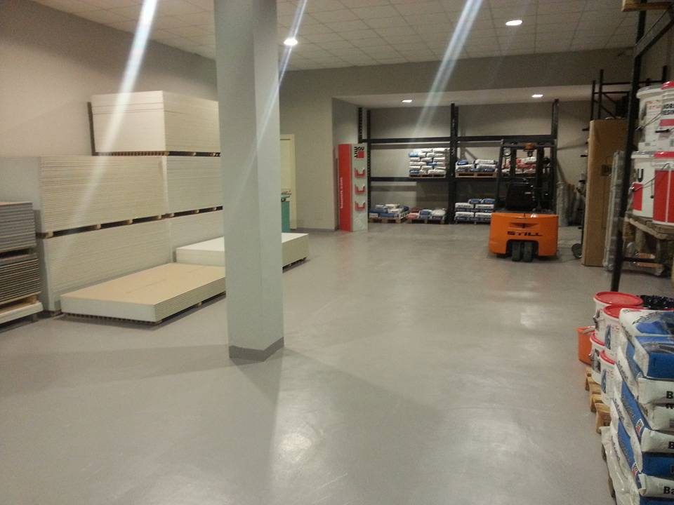 Magazzino Tecnoedil con lastre di cartongesso su pallet, sacchi di malta, secchi rossi e muletto arancione Still